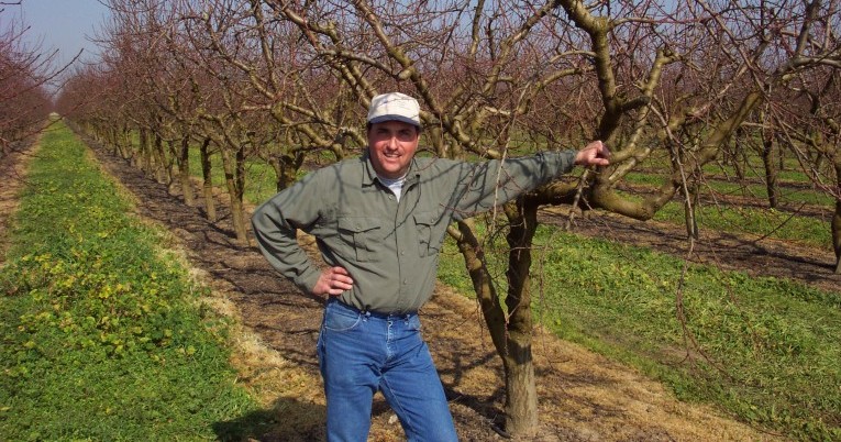 Scott Long standing in an orchard holding an apple.