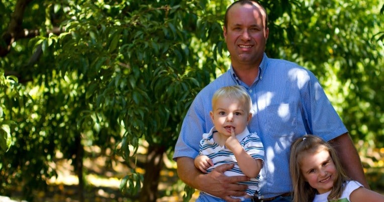 Anthony Laney and his two children standing in an orchard.