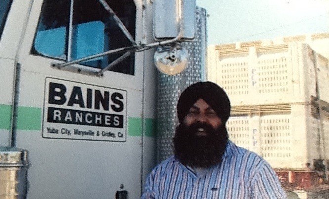 A man named Karm Bains standing in front of a truck that says Bains Ranches.