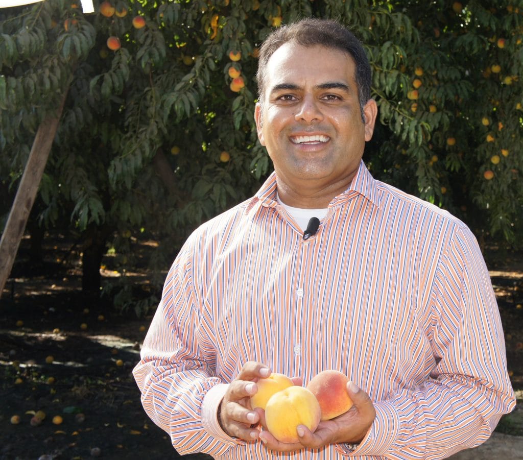 A man holding two peaches in front of a peach tree.