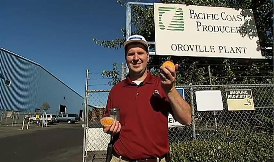 A man holding an orange can in front of a fence.