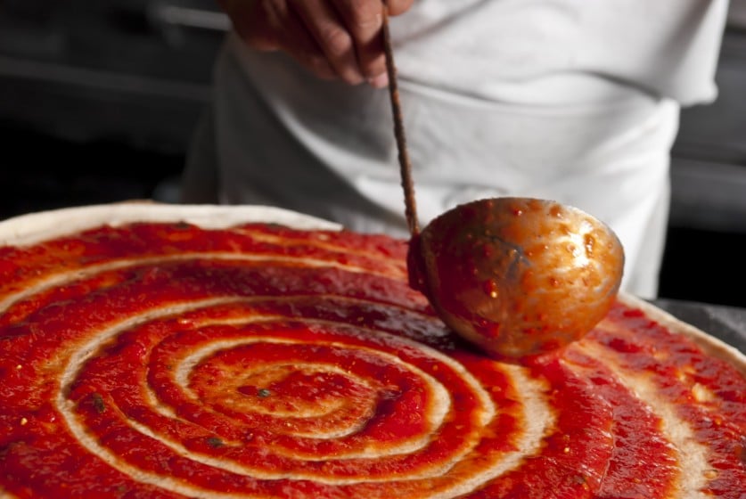 A man is making a pizza using a red sauce made by Pacific Coast Producers.