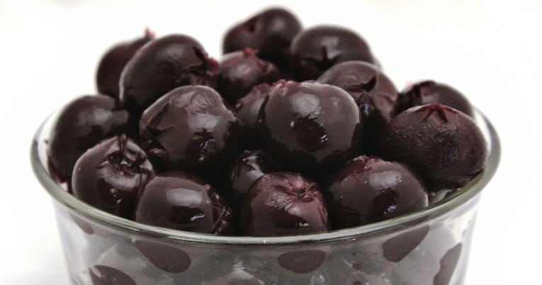 Black olives in a glass bowl on a white background.