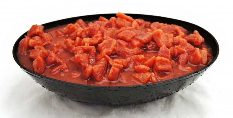 A bowl of diced pear tomatoes in juice on a white surface.