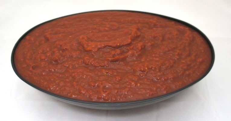 Red sauce in a bowl with #10 Ground Peeled Pear Tomatoes in Puree on a white background.
