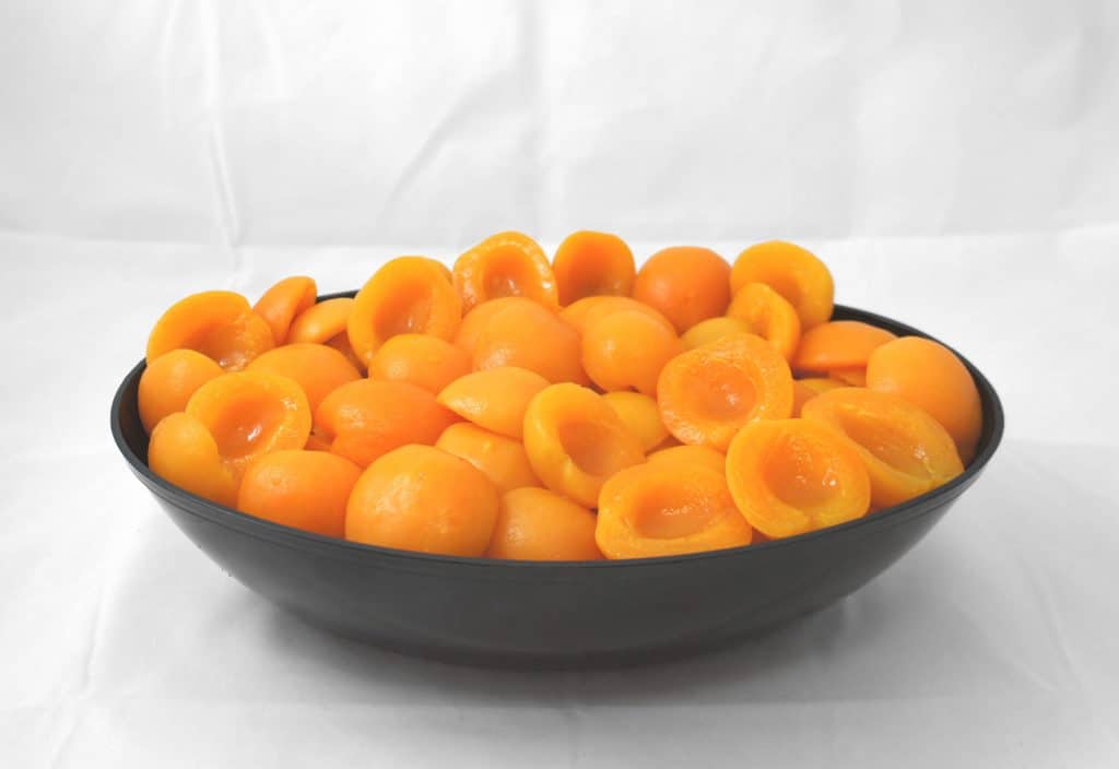 A bowl full of apricots on a white surface.