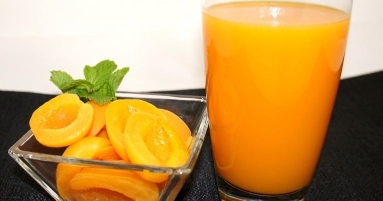 A glass of orange juice next to a bowl of apricots and 46 oz. Apricot Nectar - Fresh Pack.