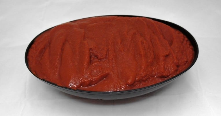 Red sauce in a bowl on a white surface.