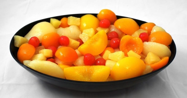 A bowl of quartered fruits in a black bowl.