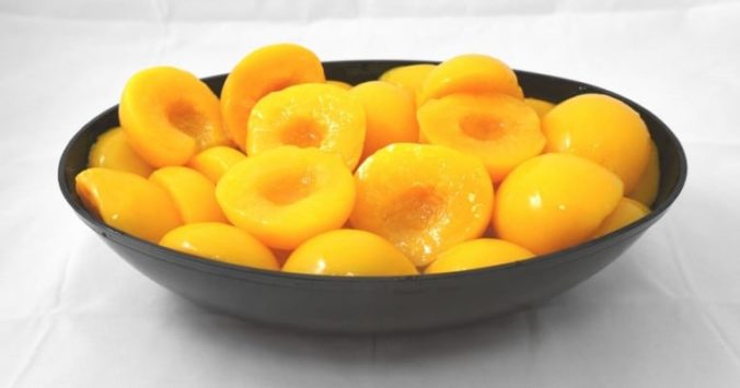A bowl of sliced apricots in heavy syrup on a white surface.