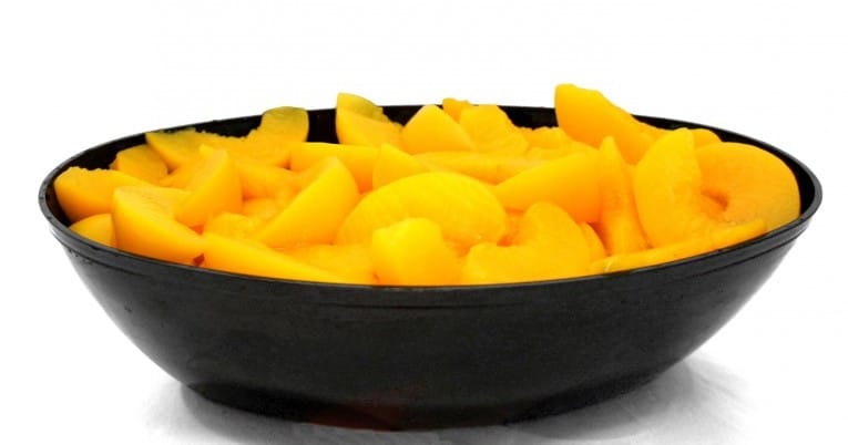 Sliced peaches in a bowl on a white background.