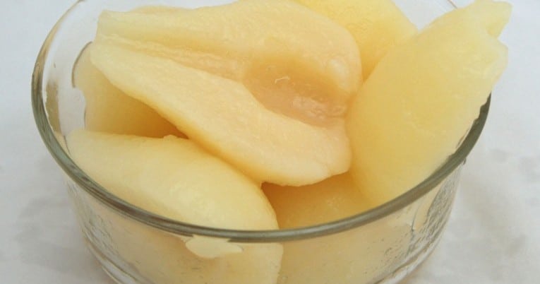Sliced apples in a glass on a white surface with #10 Northwest Pear Halves in Extra Light Syrup.