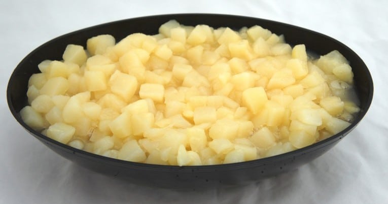 A bowl of diced potatoes on a white surface.