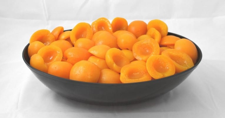 A bowl full of apricots on a white background.