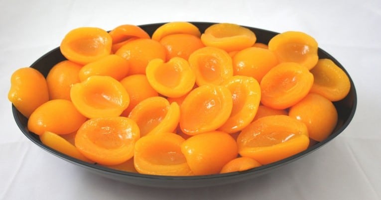 A bowl full of ripe apricots on a white surface.