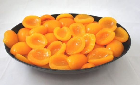 A bowl full of apricots in light syrup on a white surface.