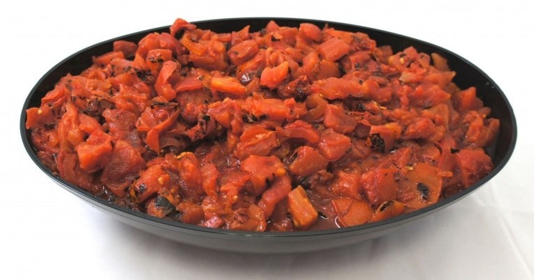 A bowl full of fire-roasted diced tomatoes in juice on a white surface.