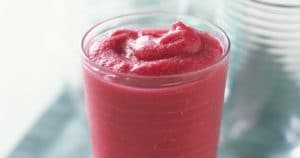 A creamy pink frappe with pears and berries served in a glass on a table.