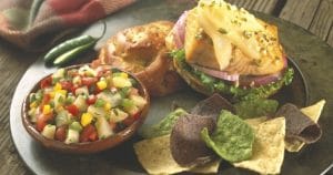 A plate with salmon burgers, chips and salsa served with Cuban pear mojo sauce.