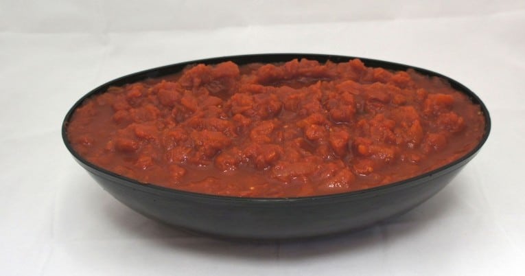 A bowl of tomato sauce on a white surface.