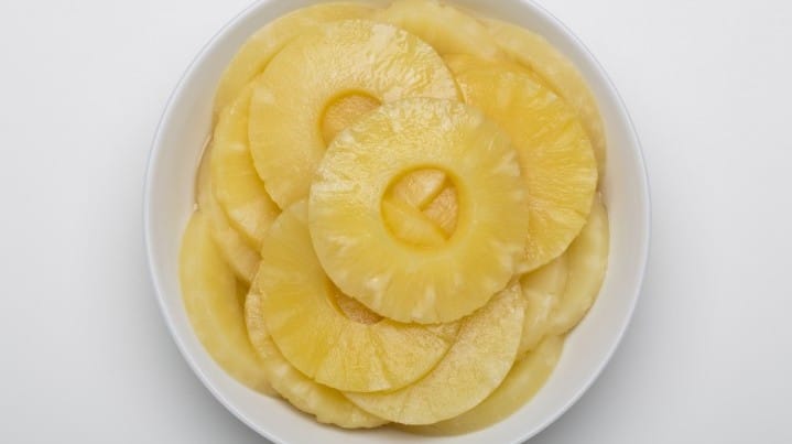 Pineapple slices in heavy syrup displayed in a white bowl.