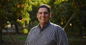 A man smiling in front of an orchard.