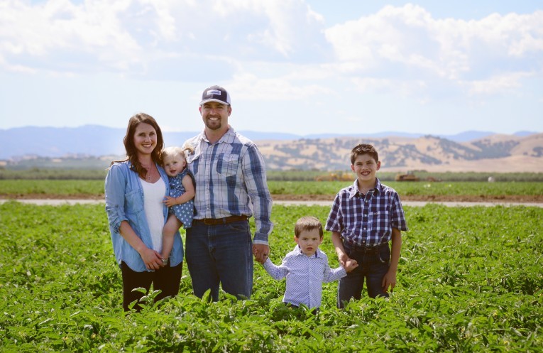 A family, captured by Colin C. Muller, stands in a field with mountains in the background.