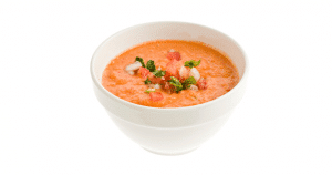 Tomato soup in a white cup on a white background.