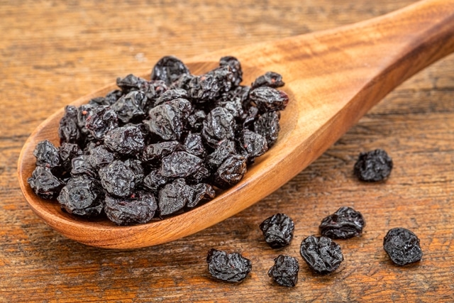Black raisins and dried cherries in a wooden spoon on a wooden table.