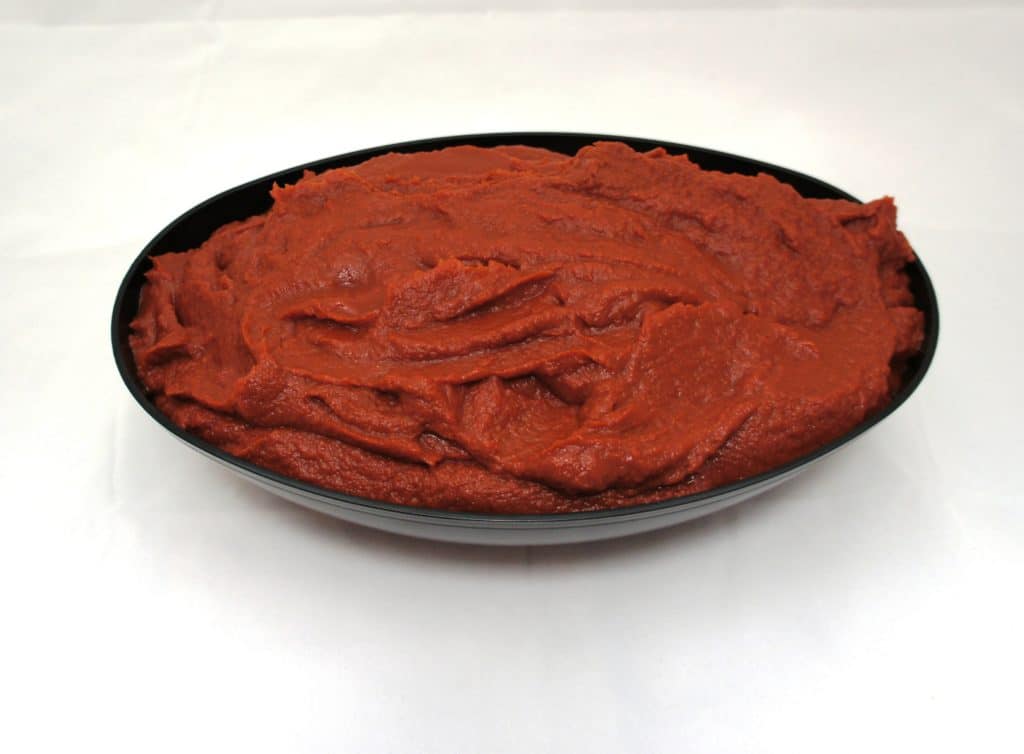A bowl of red mashed potatoes on a white surface topped with #10 Pear Tomato Puree.