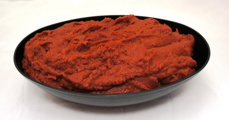 A bowl of mashed potatoes with a concentrated red tomato sauce atop, placed on a white surface.