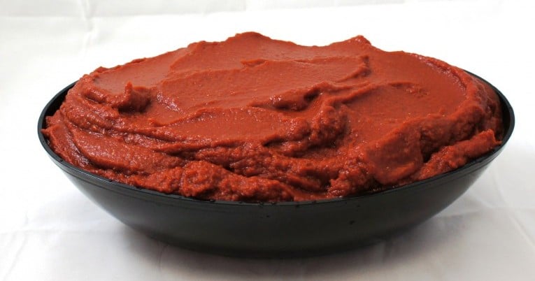 A superb bowl of red sauce in a black bowl, made with plum tomatoes and dried basil leaves.