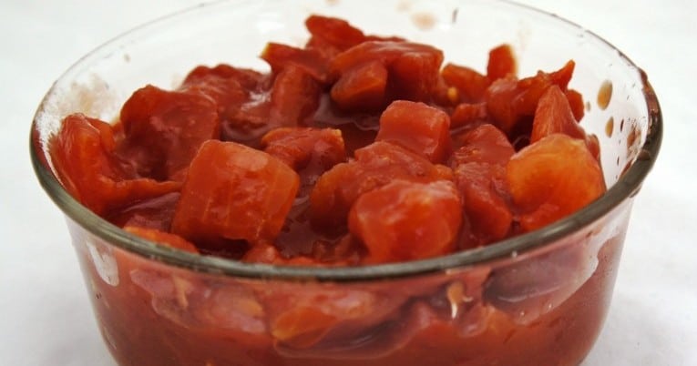 Large diced tomatoes in juice displayed in a glass bowl.