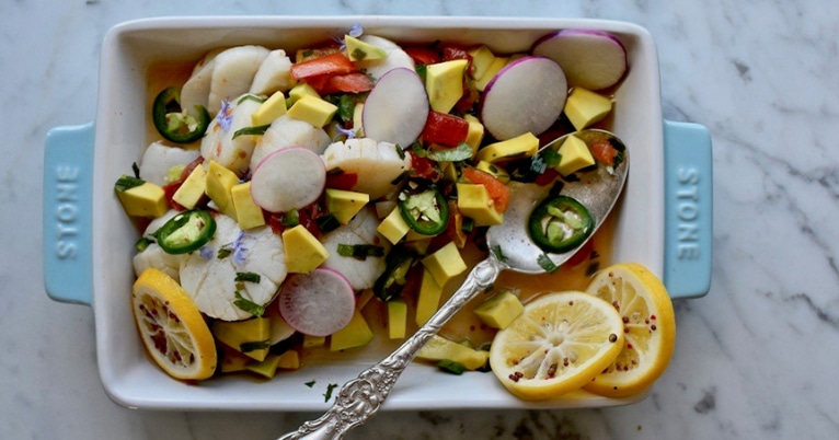 A white dish with radishes and lemons on it, garnished with Foolproof Scallops.