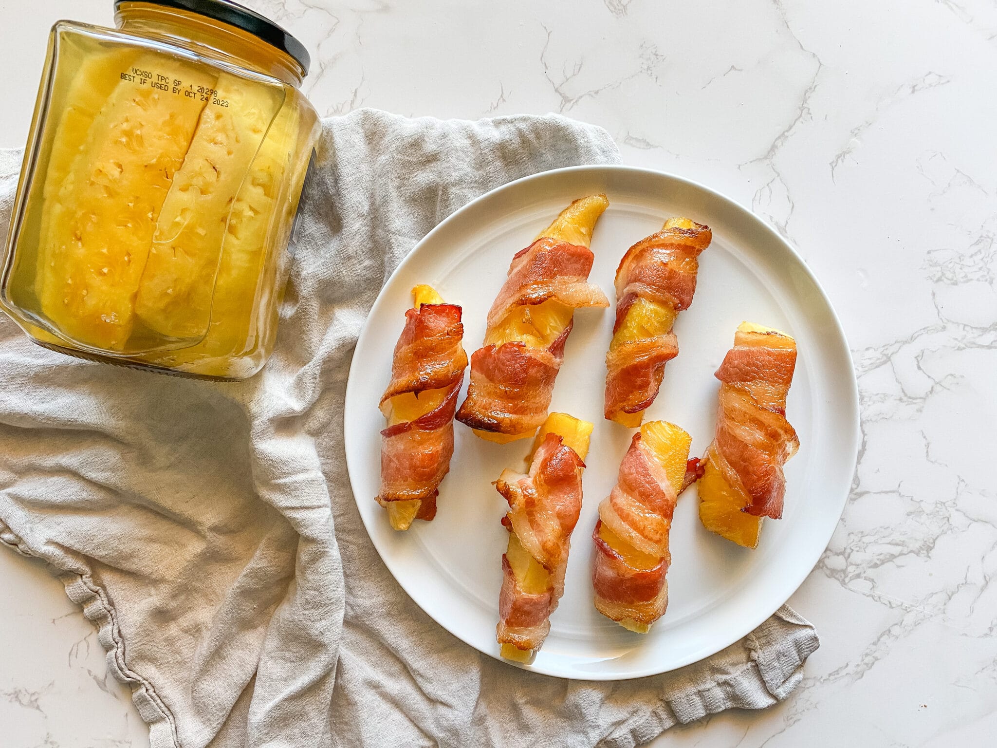 Bacon wrapped pineapples on a plate next to a jar.