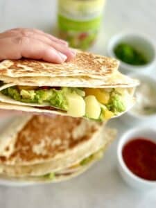 A person holding a quesadilla with guacamole and salsa.