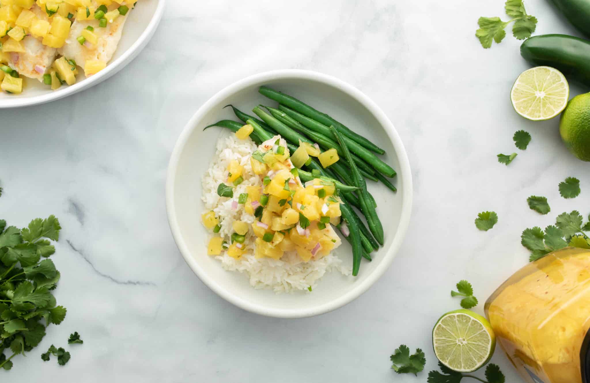 Two bowls of rice, green beans and pineapple on a marble table.