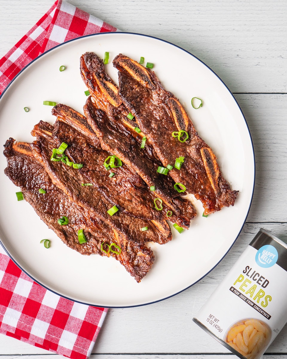 Beef ribs on a plate next to a can of ketchup.