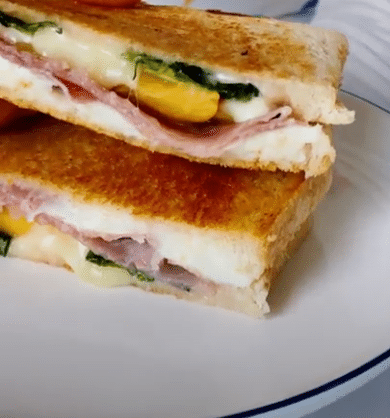 A grilled cheese sandwich with ham and spinach on a plate.